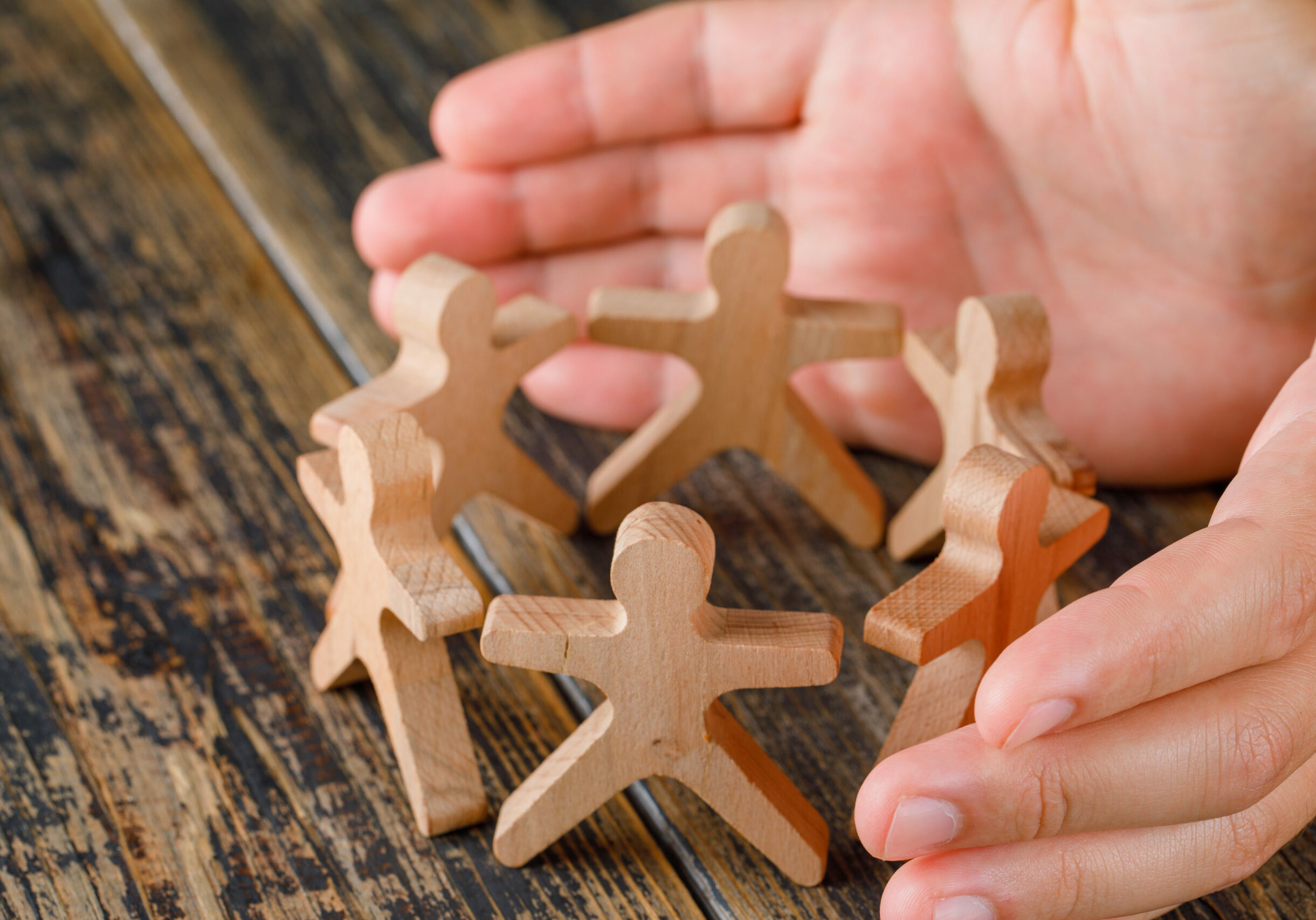Business success concept on wooden background high angle view. hands protecting wooden figures of people.